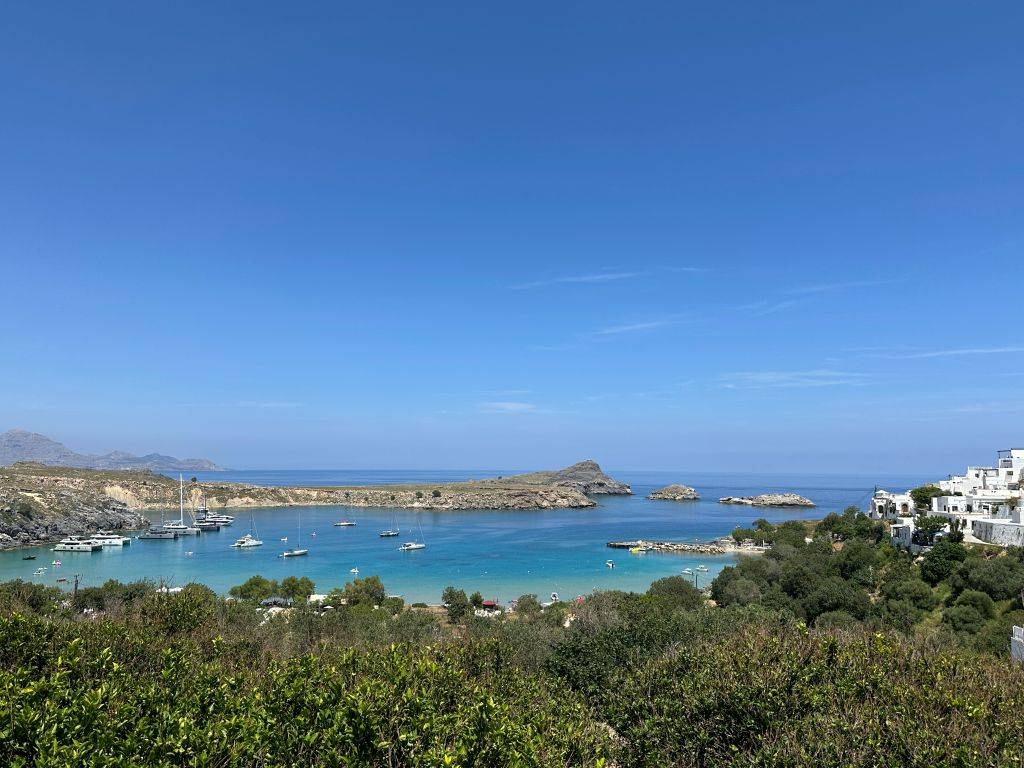 Panoramablick auf die Bucht von Lindos mit türkisblauem Wasser, felsiger Küste und mediterraner Landschaft auf der Insel Rhodos.