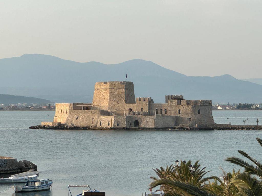 Bourtzi Festung im Hafen von Nafplio mit kleinem Boot im Vordergrund und Bergen im Hintergrund in Griechenland