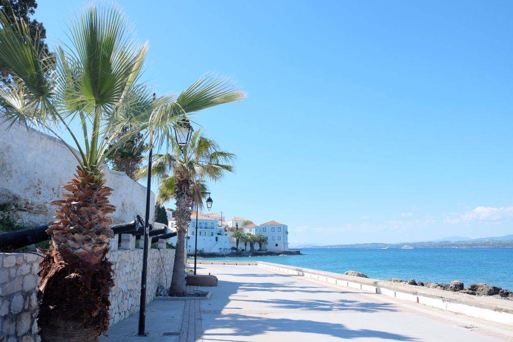 Küstenweg auf Spetses mit Palmen und Blick auf ein traditionelles Haus nahe Dapia und dem Meer